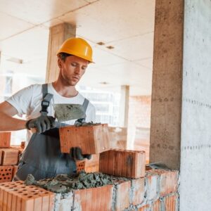 maurer Mann macht mit einer Kelle Mörtel auf einen Stein