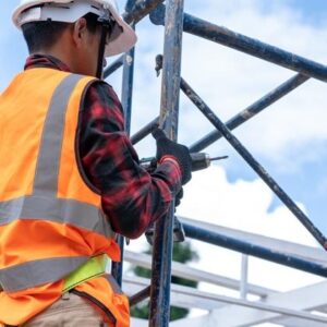 Mann mit Akkuschrauber in der Hand steht auf einem Gerüst
