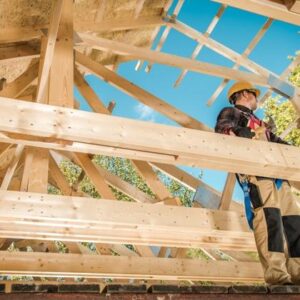 Mann mit Hammer in der Hand steht auf dem Dachstuhl